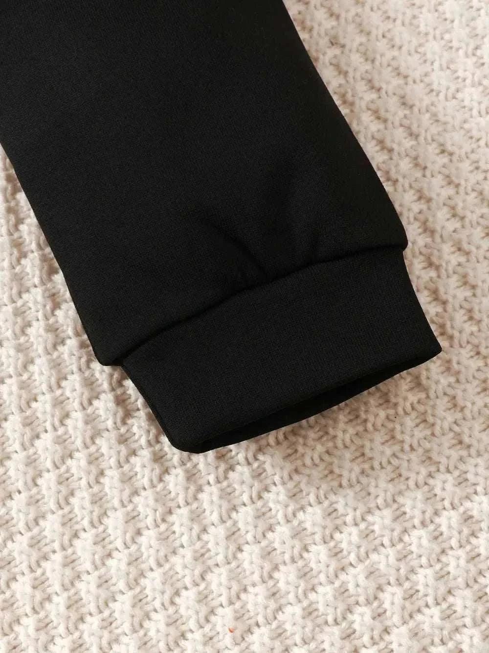 Close-up of black fabric cuff from children's dinosaur sweatshirt set on textured surface