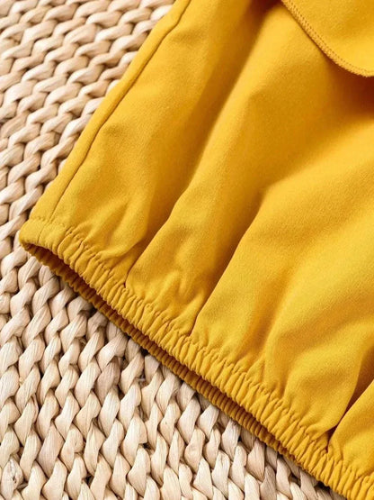 Close-up of yellow children's ruffled spaghetti strap top with elastic hem on woven background