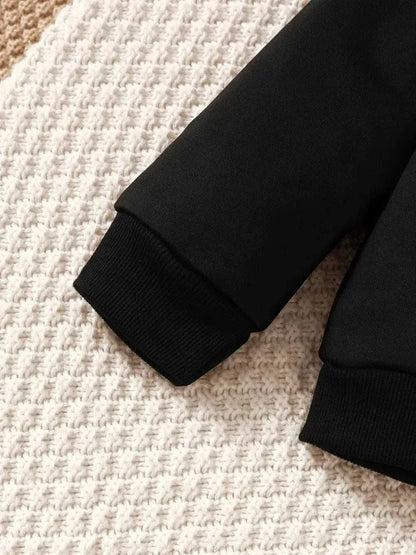 Close-up of black ribbed cuffs on children's dinosaur sweatshirt set sleeve on textured background