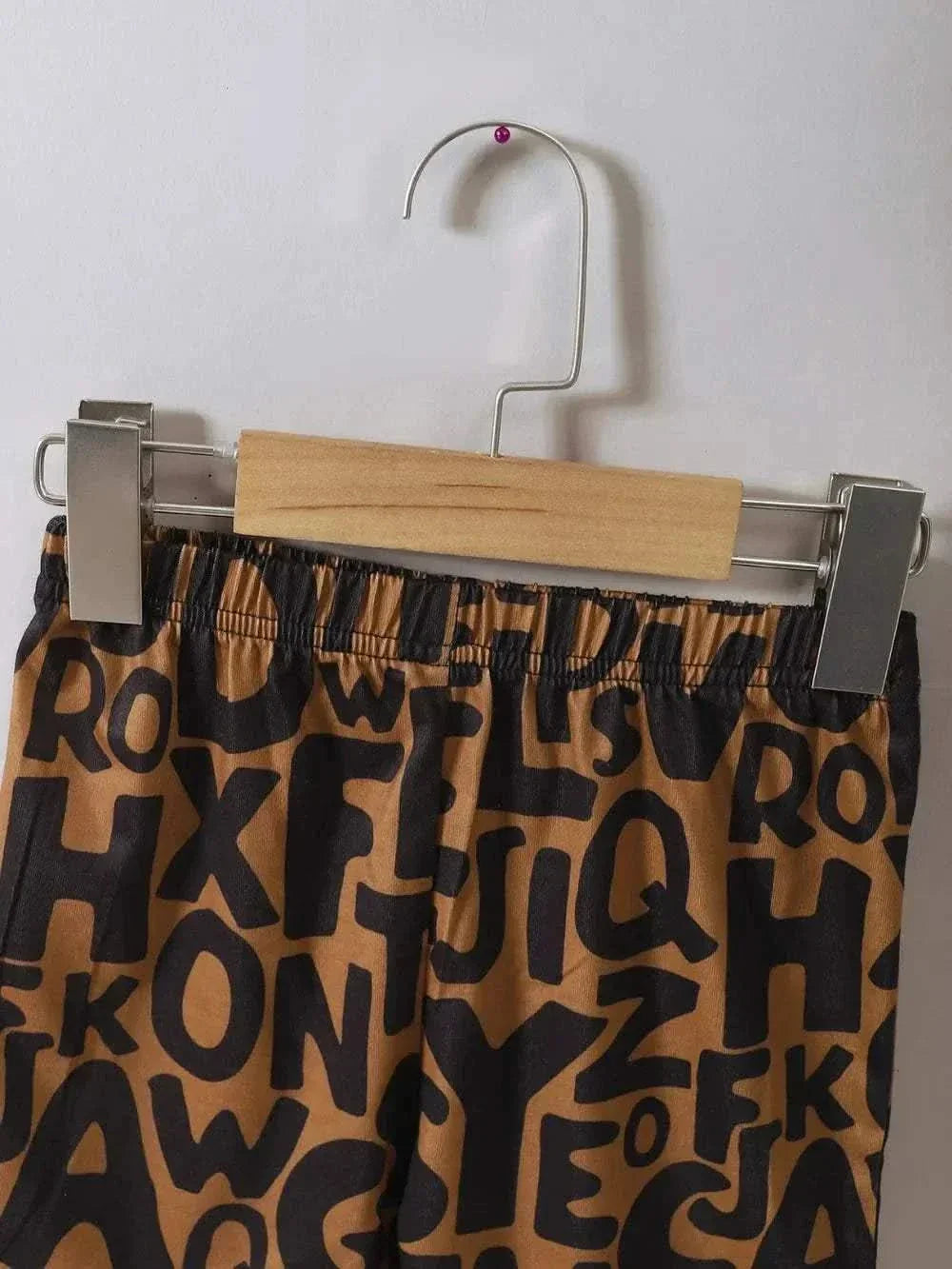 Children's Teddy Bear Round Neck Top and Pants Set featuring brown pants with black alphabet print hanging on wooden hanger.