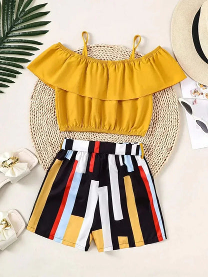 Children's ruffled yellow spaghetti strap top with multicolor striped shorts set laid on woven mat with summer accessories