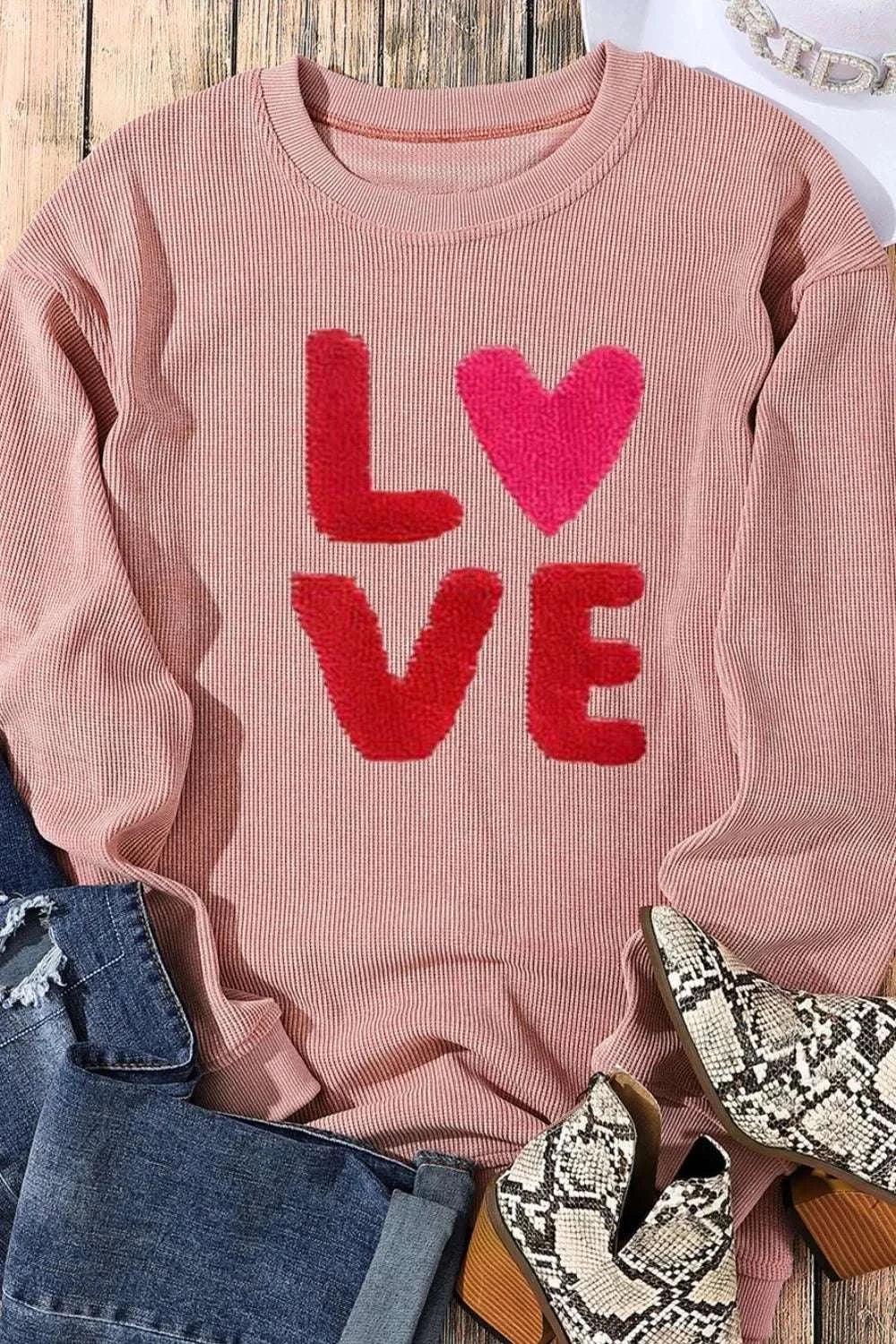 Valentine’s Day LOVE pink long sleeve sweatshirt with red and pink heart design, paired with denim jeans and snake print boots